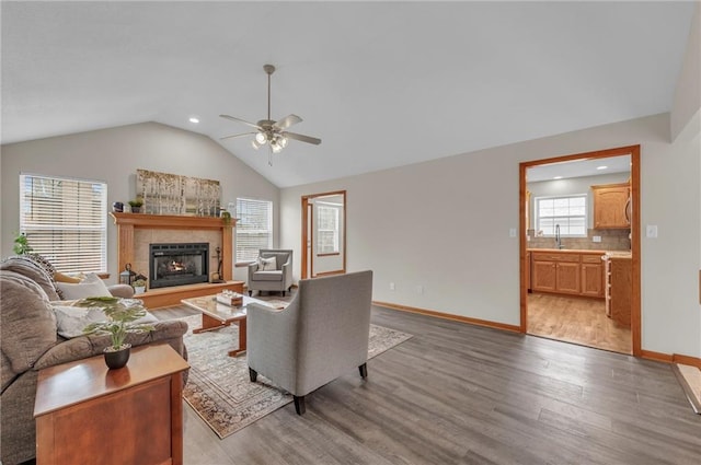 living room featuring light wood finished floors, baseboards, ceiling fan, vaulted ceiling, and a fireplace