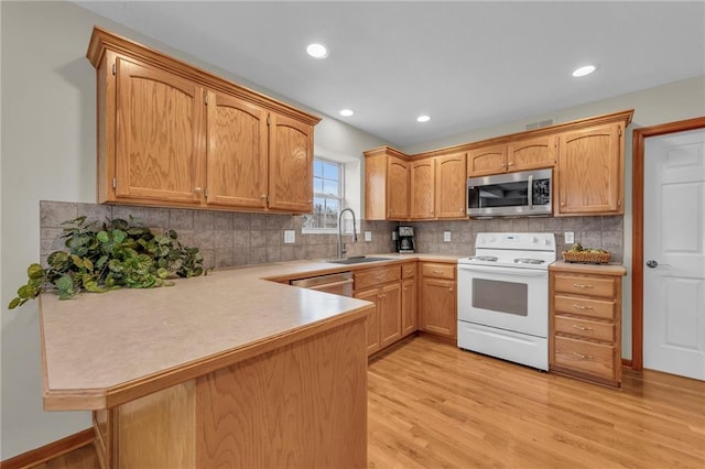 kitchen with a peninsula, a sink, light wood-style floors, light countertops, and appliances with stainless steel finishes