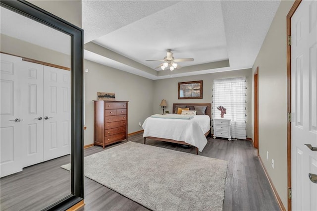 bedroom featuring a textured ceiling, a closet, a raised ceiling, and dark wood finished floors