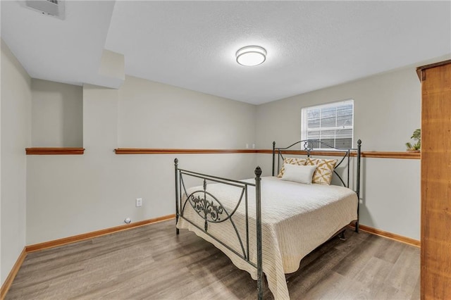 bedroom with a textured ceiling, baseboards, and wood finished floors