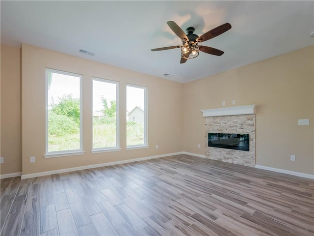 unfurnished living room with visible vents, baseboards, a ceiling fan, light wood-style flooring, and a stone fireplace