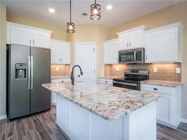 kitchen with stainless steel appliances, a sink, white cabinets, hanging light fixtures, and a center island with sink