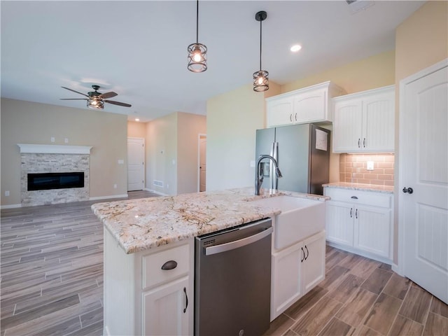 kitchen with a center island with sink, white cabinetry, stainless steel appliances, and decorative light fixtures