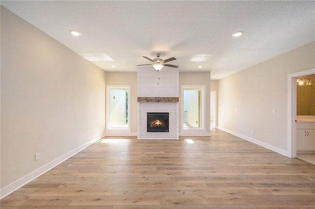 unfurnished living room featuring light hardwood / wood-style flooring, a large fireplace, and ceiling fan