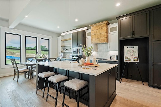 kitchen featuring light hardwood / wood-style flooring, a kitchen island with sink, hanging light fixtures, a kitchen breakfast bar, and decorative backsplash