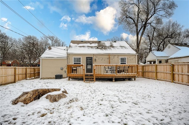 snow covered house with a fenced backyard and a deck