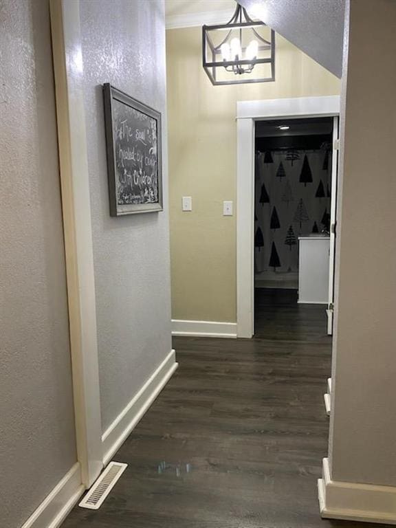 corridor featuring dark wood-type flooring, vaulted ceiling, and an inviting chandelier