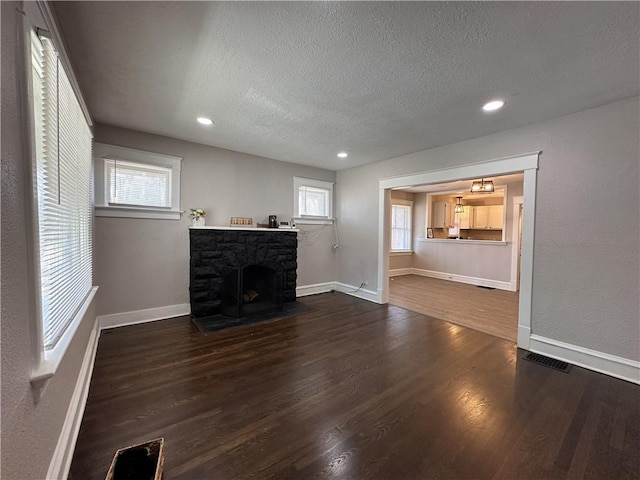 unfurnished living room featuring a textured ceiling, a stone fireplace, dark wood-style flooring, visible vents, and baseboards