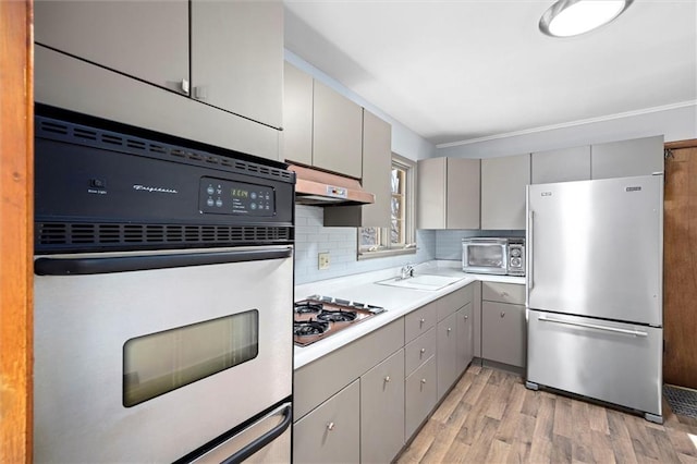 kitchen featuring gray cabinets, freestanding refrigerator, a sink, oven, and under cabinet range hood