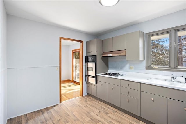 kitchen featuring stainless steel appliances, gray cabinets, under cabinet range hood, a sink, and a warming drawer