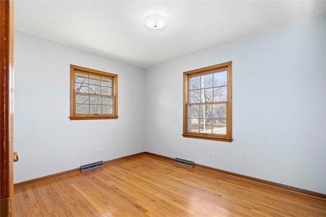 spare room featuring light wood finished floors, visible vents, and baseboards