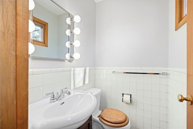 half bathroom with wainscoting, a sink, tile walls, and toilet