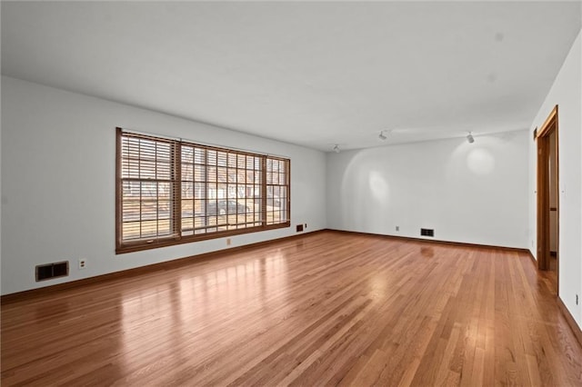 spare room featuring light wood-style flooring, visible vents, and baseboards