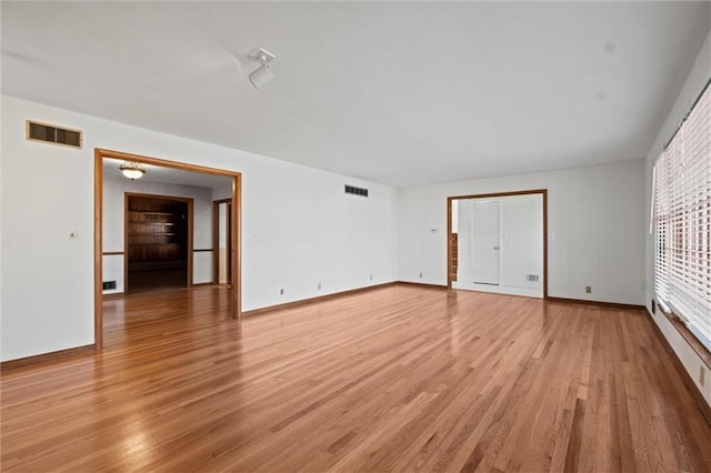 empty room with light wood finished floors, visible vents, and baseboards