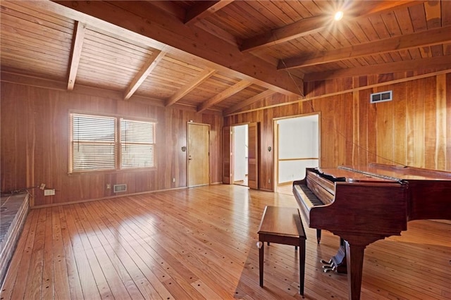 unfurnished room with visible vents, vaulted ceiling with beams, wooden walls, and hardwood / wood-style floors