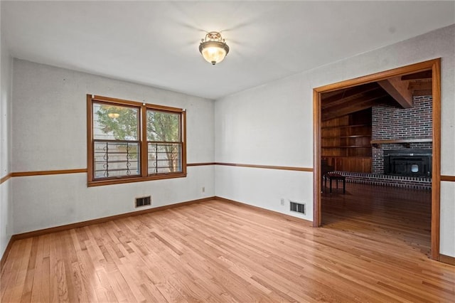 unfurnished room with a large fireplace, built in shelves, light wood-type flooring, and visible vents