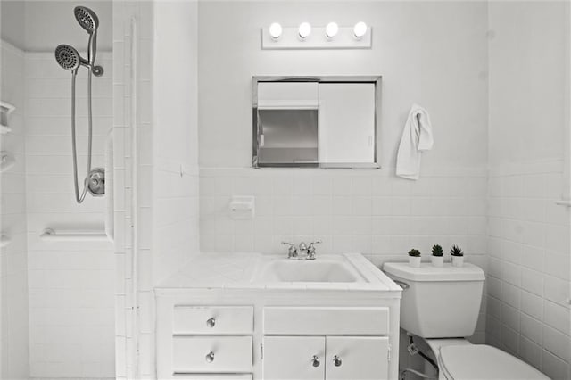 full bathroom with vanity, a tile shower, toilet, and tile walls