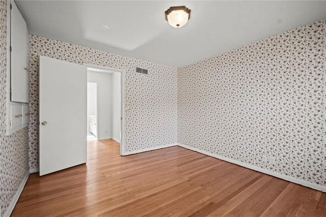 unfurnished room with light wood-type flooring, visible vents, and wallpapered walls