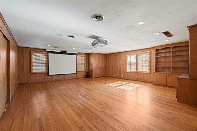 home theater room with wooden walls, visible vents, and light wood-style flooring