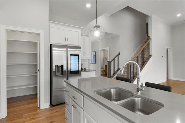 kitchen featuring hanging light fixtures, light wood-style floors, white cabinetry, a sink, and stainless steel fridge