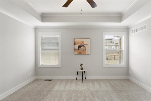 unfurnished room featuring a tray ceiling, visible vents, crown molding, and light carpet