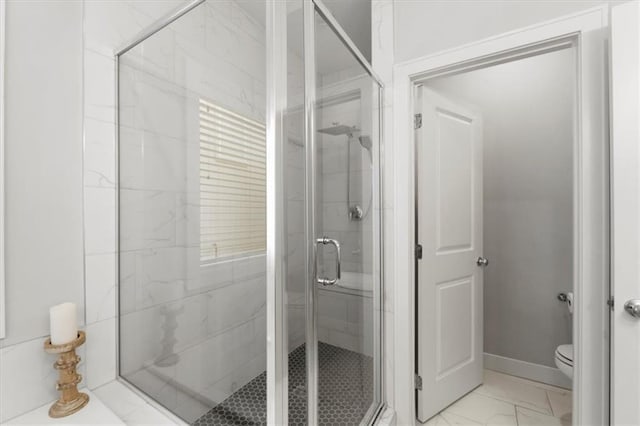 bathroom with toilet, marble finish floor, baseboards, and a stall shower