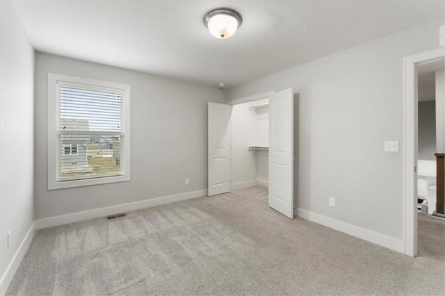 unfurnished bedroom featuring visible vents, baseboards, light colored carpet, a spacious closet, and a closet