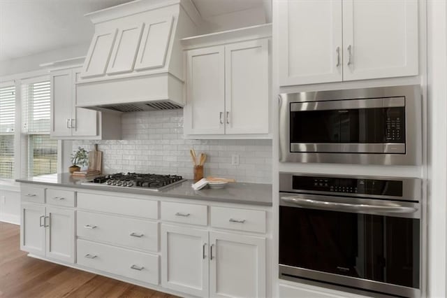 kitchen featuring stainless steel appliances, light countertops, light wood-style flooring, decorative backsplash, and white cabinetry