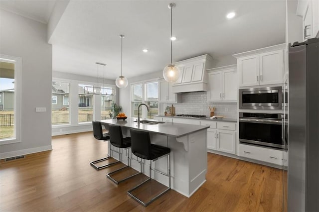 kitchen with stainless steel appliances, a sink, custom range hood, white cabinets, and recessed lighting
