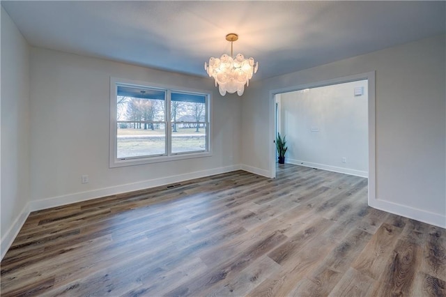 spare room featuring a chandelier, baseboards, and wood finished floors