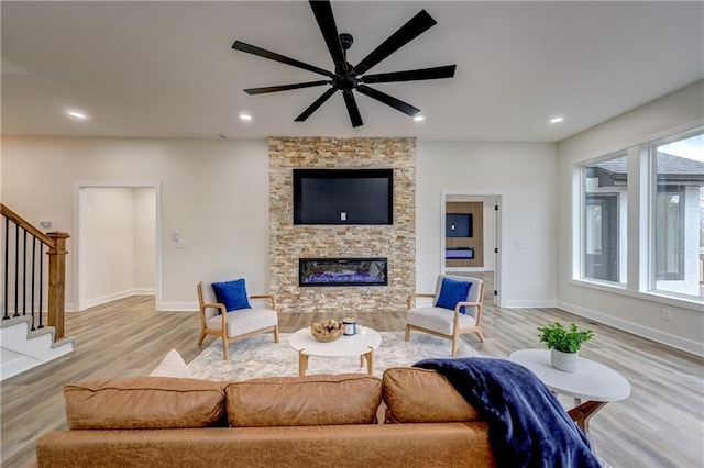 living area featuring baseboards, a fireplace, light wood finished floors, and stairs