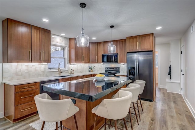 kitchen featuring a breakfast bar area, a sink, appliances with stainless steel finishes, light wood finished floors, and brown cabinetry