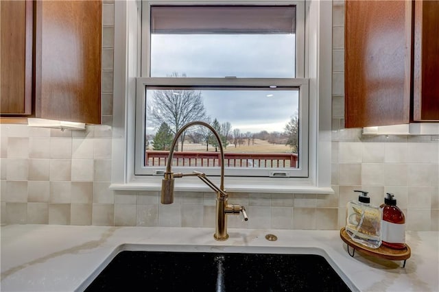 room details featuring brown cabinetry, a sink, light stone countertops, and decorative backsplash