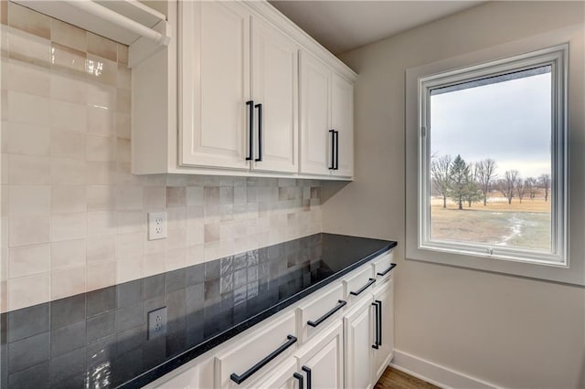 kitchen featuring dark stone countertops, tasteful backsplash, white cabinetry, and baseboards