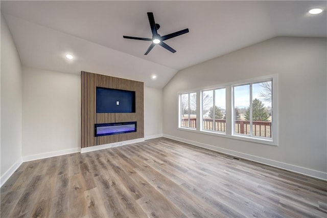 unfurnished living room with a large fireplace, baseboards, vaulted ceiling, and wood finished floors