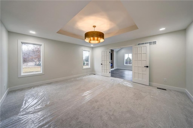 carpeted empty room with french doors, a raised ceiling, visible vents, and baseboards