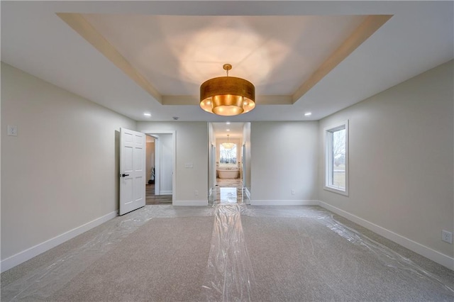 empty room featuring light carpet, recessed lighting, a raised ceiling, and baseboards