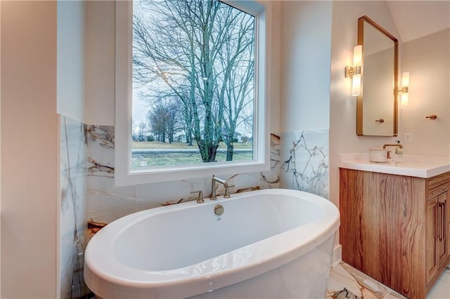 full bathroom featuring marble finish floor, a freestanding bath, and vanity