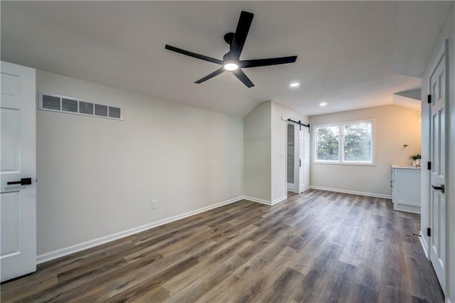 unfurnished bedroom with a barn door, baseboards, visible vents, dark wood-type flooring, and vaulted ceiling