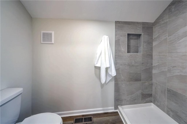 full bathroom with toilet, a tile shower, visible vents, and baseboards