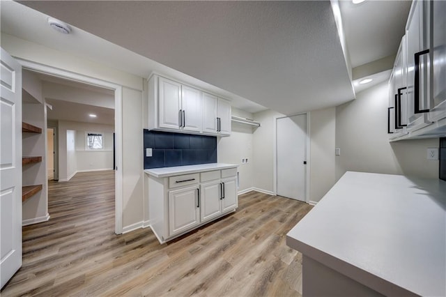 kitchen featuring white cabinets, light countertops, backsplash, and light wood finished floors