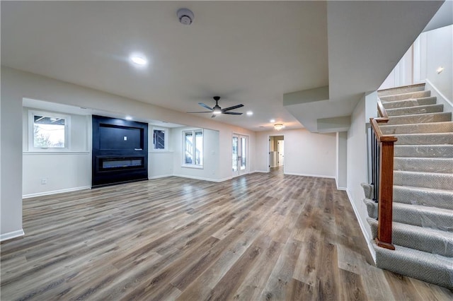 unfurnished living room featuring stairs, a fireplace, wood finished floors, and baseboards