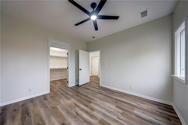 unfurnished bedroom featuring visible vents, baseboards, a walk in closet, and wood finished floors