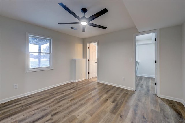 unfurnished bedroom with baseboards, visible vents, a ceiling fan, wood finished floors, and a walk in closet