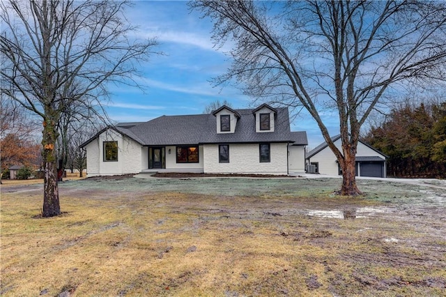 view of front facade with roof with shingles, a front yard, a detached garage, and an outdoor structure