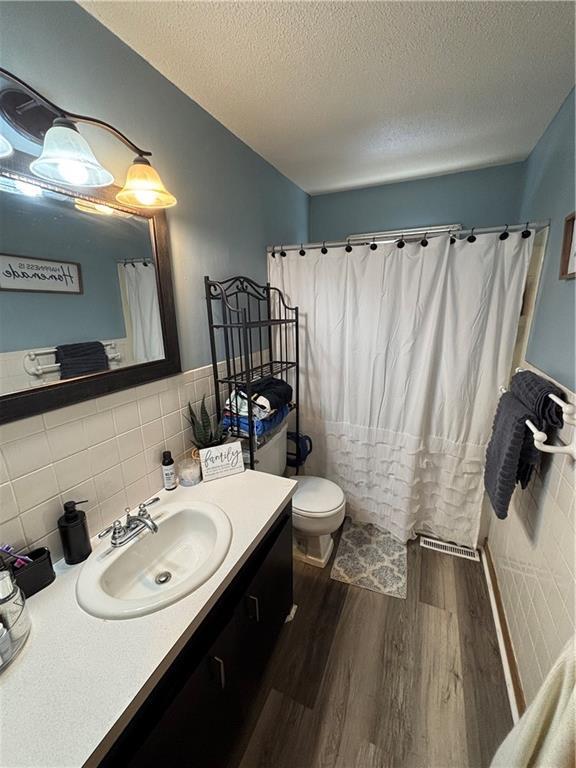 bathroom featuring hardwood / wood-style flooring, tile walls, vanity, a textured ceiling, and toilet