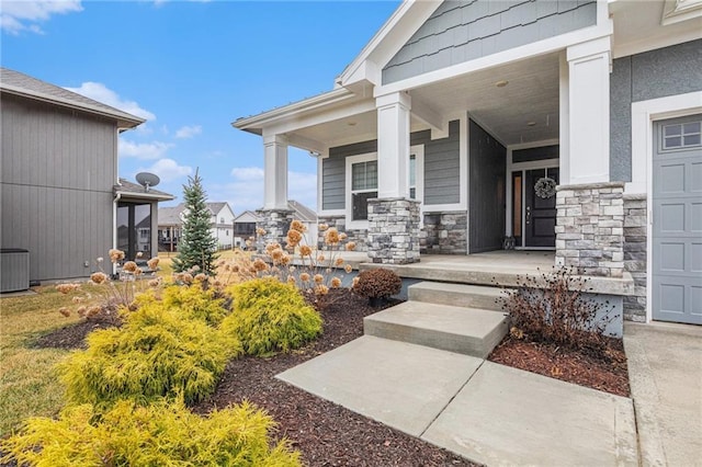 property entrance with covered porch, stone siding, and a garage