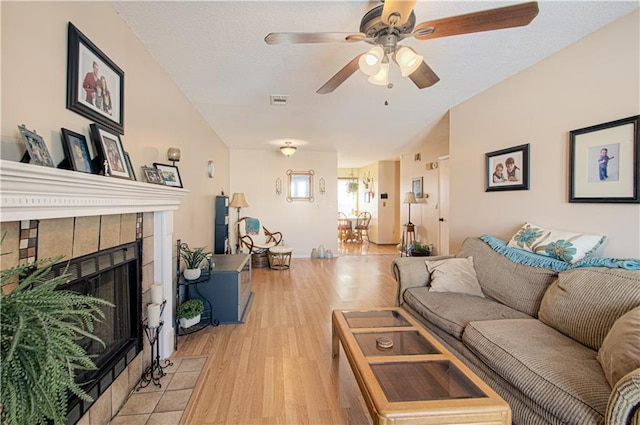 living room featuring light wood-type flooring, a ceiling fan, visible vents, and a tiled fireplace