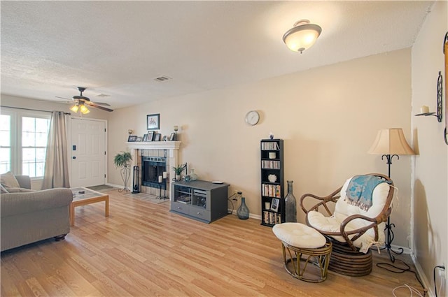 living room featuring a ceiling fan, light wood-type flooring, baseboards, and a tile fireplace