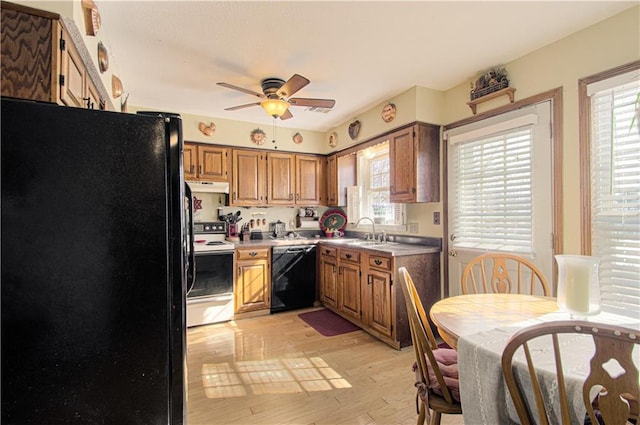 kitchen featuring brown cabinets, under cabinet range hood, light countertops, black appliances, and a sink